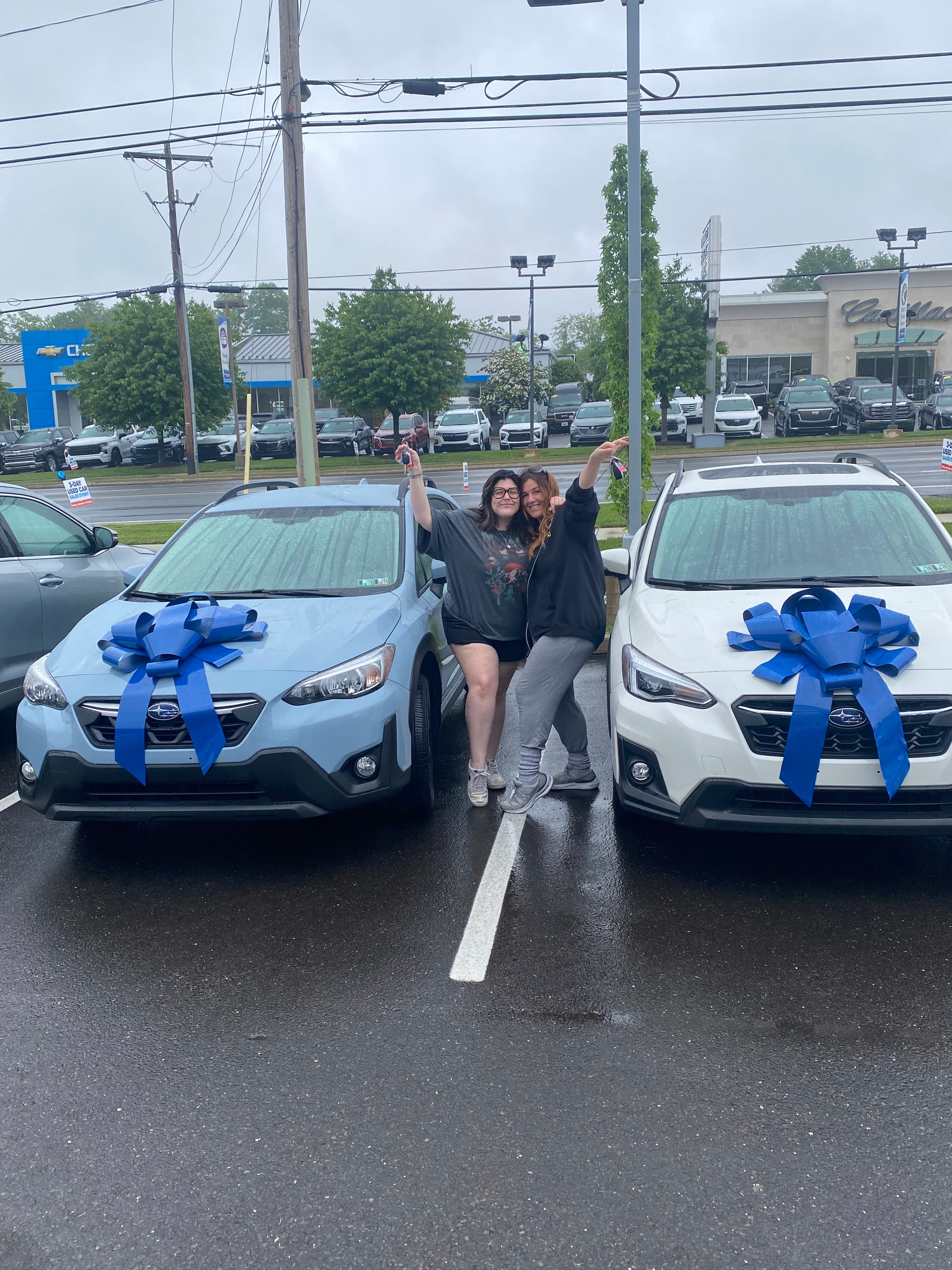 Two women celebrate holding keys between two new Subarus with large blue gift bows.