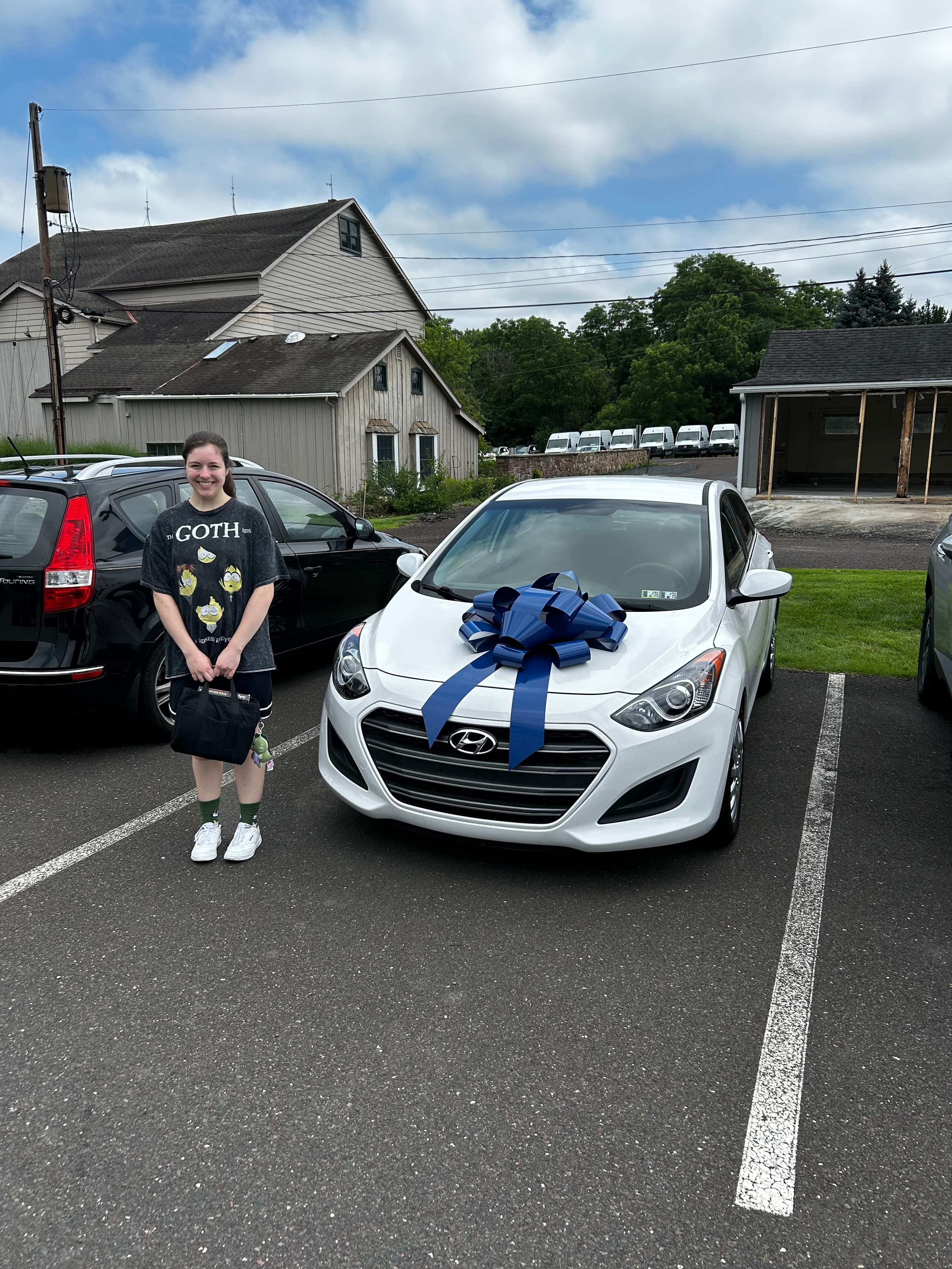 Smiling person stands beside a white Hyundai car with a large blue gift bow.